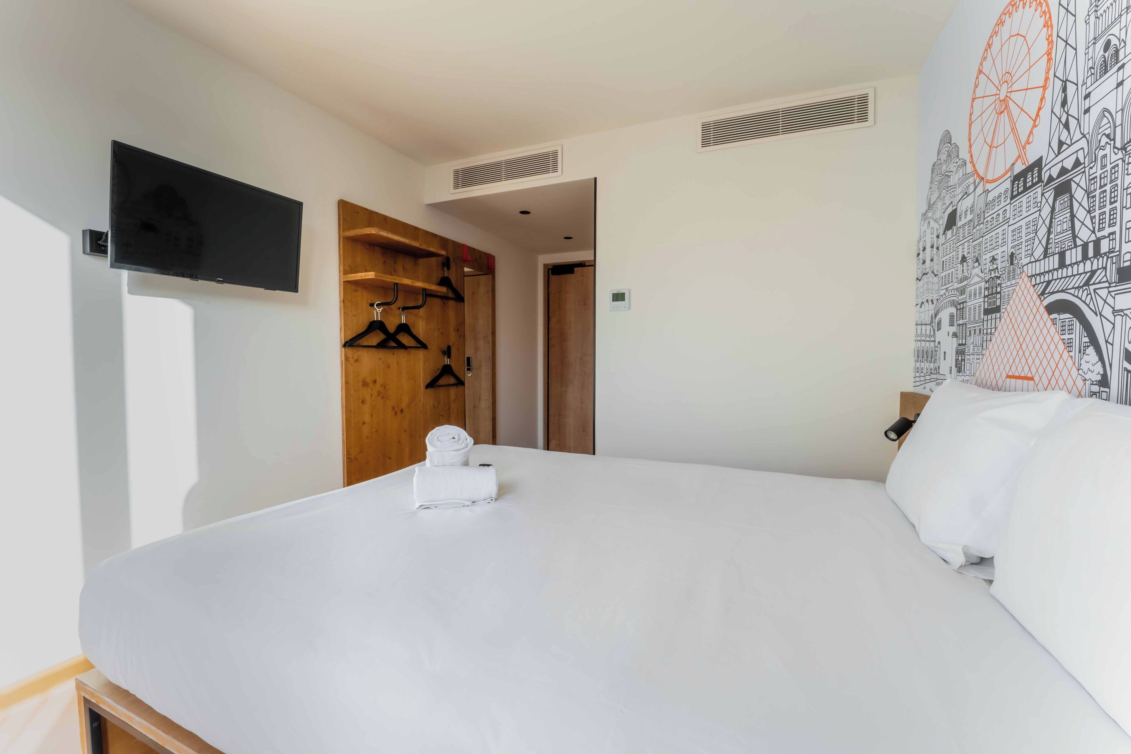 A hotel room with a large bed, a flat-screen TV mounted on the wall, a wooden wardrobe, and a wall mural.