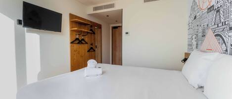 A hotel room with a large bed, a flat-screen TV mounted on the wall, a wooden wardrobe, and a wall mural.