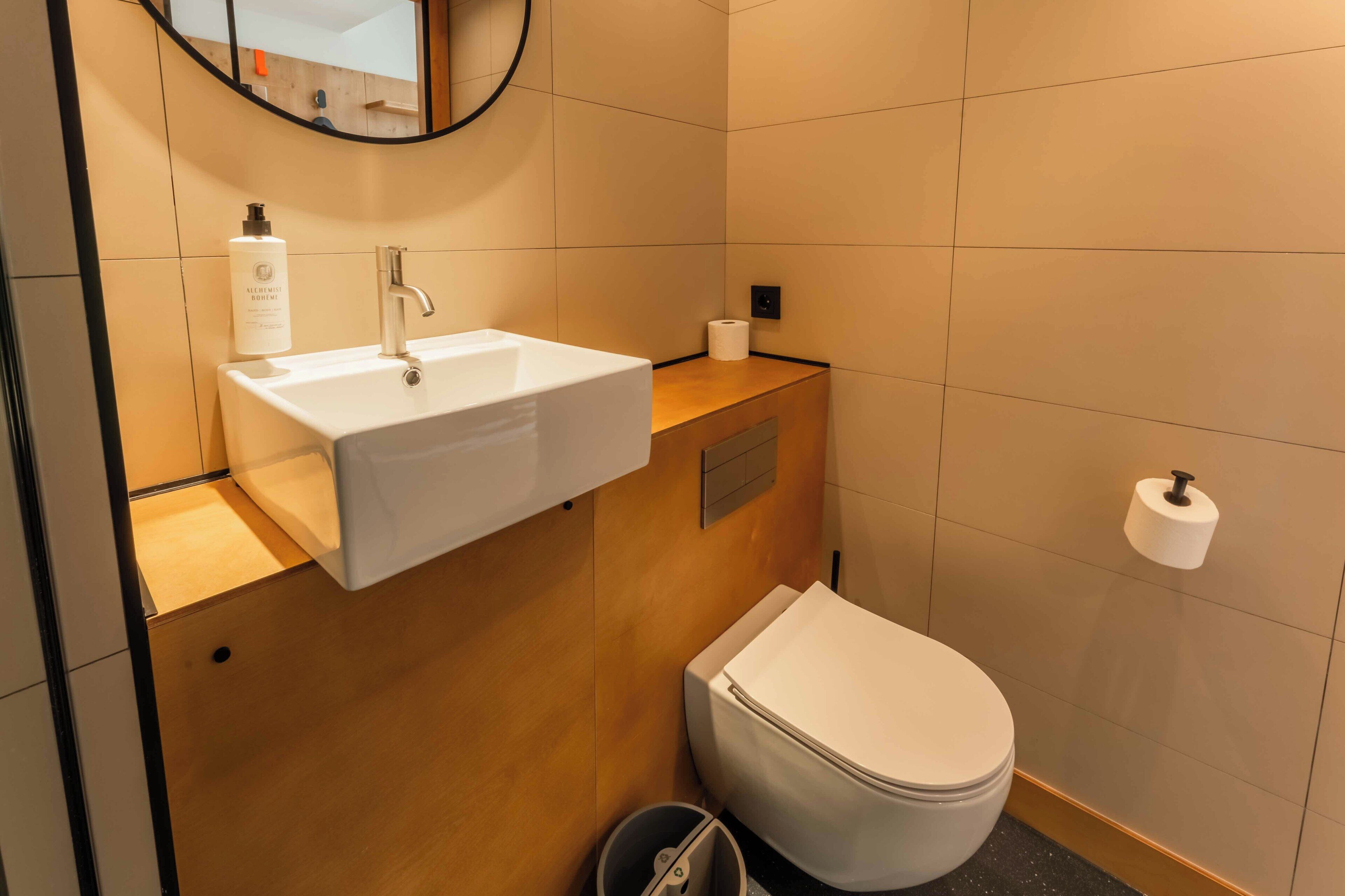 Un baño moderno con un lavamanos blanco, un inodoro y un espejo sobre el lavamanos.