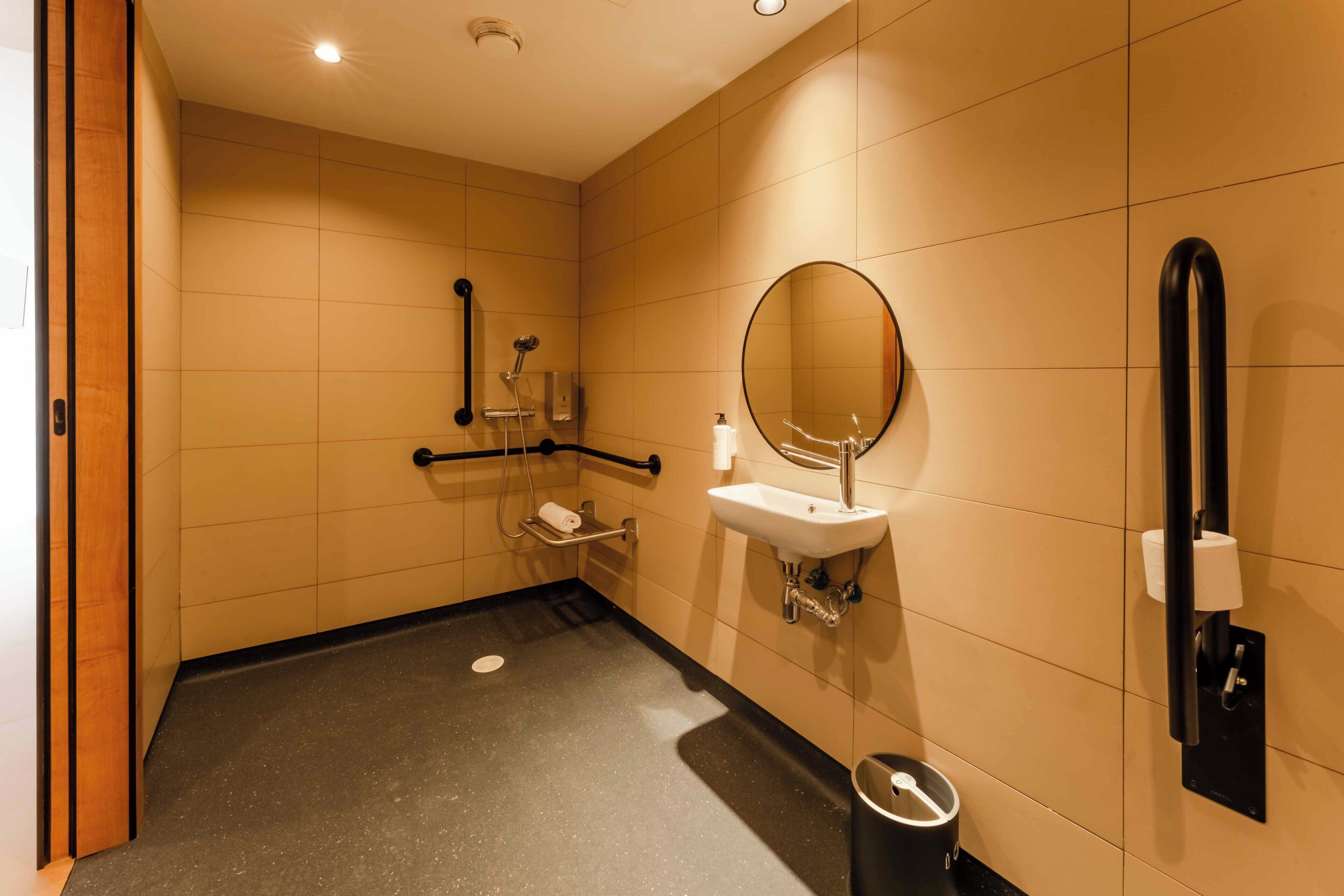 Baño con lavabo, espejo, secador de manos y cubo de basura.