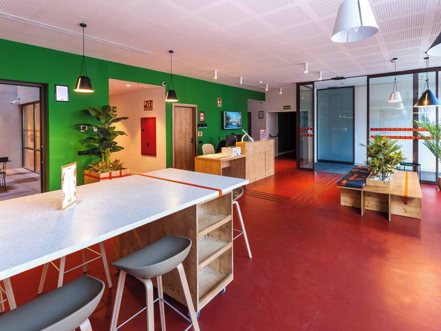 A modern reception area with a green wall, wooden reception desk, and bar stools.