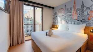 Ein Hotelzimmer mit einem großen Bett, einem Stadtbild-Wandgemälde, einem Fenster mit Vorhängen und Blick auf die Stadt.