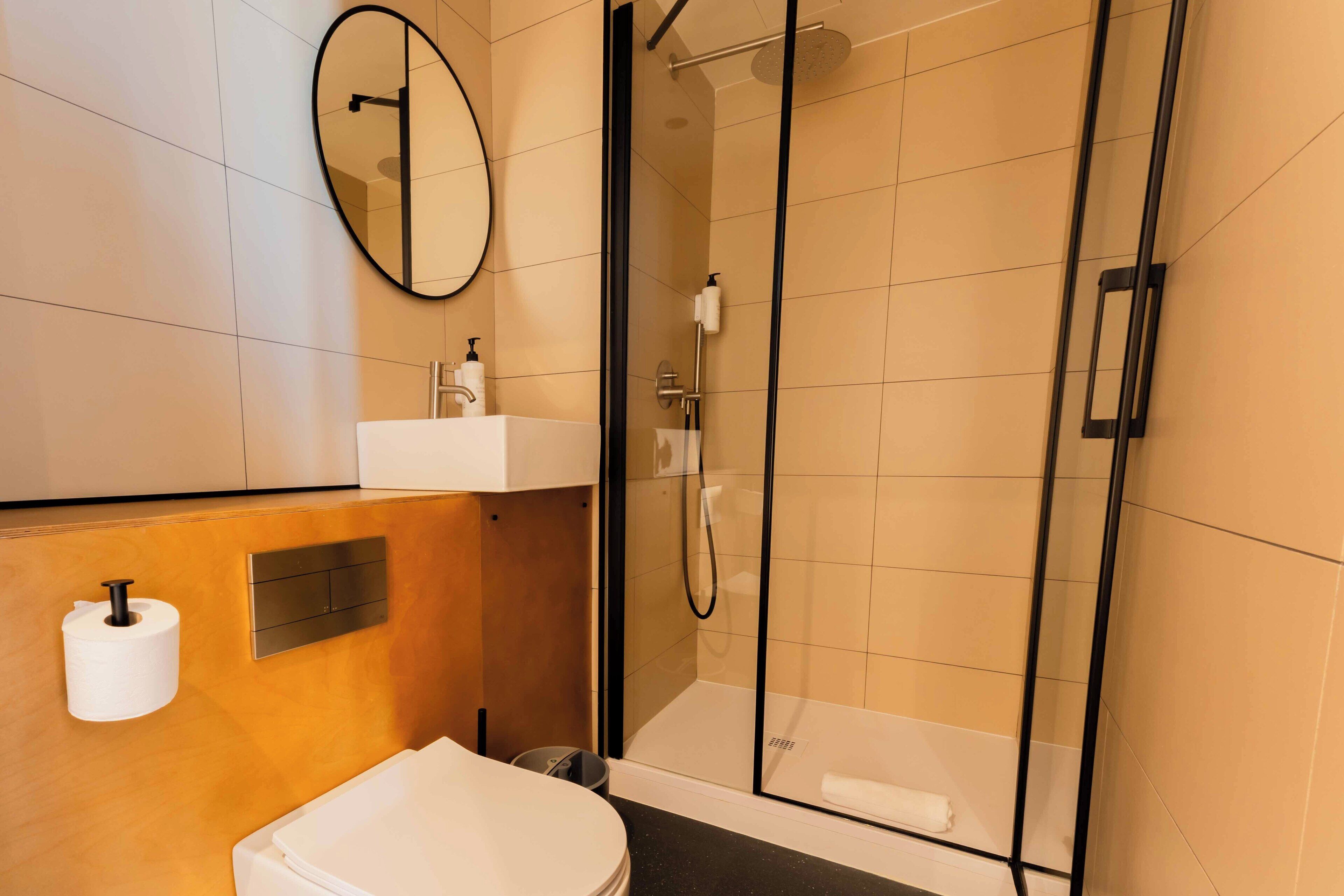Ein modernes Badezimmer mit einer Duschkabine aus Glas, einem weißen Waschbecken und einem Spiegel.