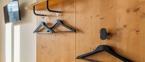 Pared de madera con un televisor montado a la izquierda, estantes de madera arriba y perchas negras colgadas en la pared.