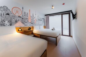 Ein Hotelzimmer mit zwei Betten, einem Stadtbild-Wandgemälde, einem großen Fenster und einer Schiebetür.