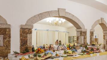 Una sala da banchetti con archi in pietra, un lampadario e un tavolo imbandito con diversi piatti.