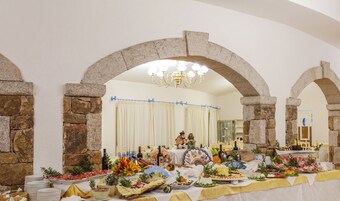 Un salón de banquetes con arcos de piedra, una araña y una mesa dispuesta con diferentes alimentos.