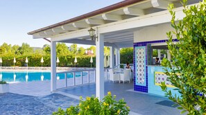 Zona de piscina con un espacio de estar techado, piscina y bar.