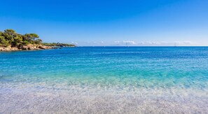 Una playa con agua turquesa cristalina, un litoral rocoso y un velero a lo lejos.