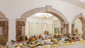 A banquet hall with stone arches, a chandelier, and a table set with various food items. - Li Cucutti (Sassari)
