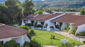 A row of white buildings with red-tiled roofs, surrounded by greenery and a mountainous backdrop. - Li Cucutti (Sassari)