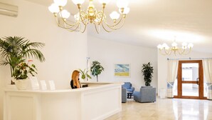 A hotel lobby with a reception desk, seating area, and a large chandelier. - Li Cucutti (Sassari)