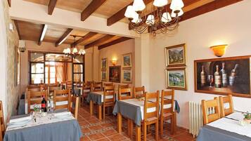 A dining area with wooden tables and chairs, a chandelier, and artwork on the walls.