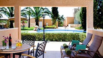 A covered outdoor area with a pool, lounge chairs, and a table with drinks and fruits.