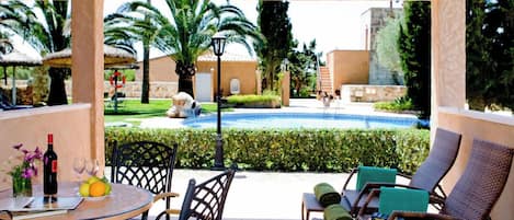 A covered outdoor area with a pool, lounge chairs, and a table with drinks and fruits.