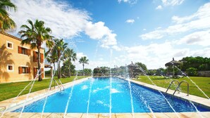 A swimming pool with water jets, surrounded by palm trees and a building with balconies. - Son Marge Sl.l (Ses Salines)