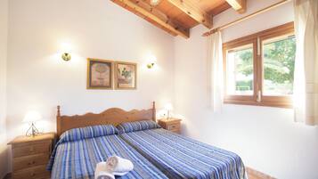 A bedroom with a wooden bed, two bedside tables with lamps, a window with curtains, and two wall-mounted light fixtures.