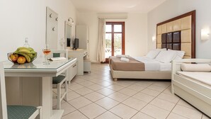 Habitación de hotel con cama, escritorio con silla, mesita con fruta y un vaso, y televisor.
