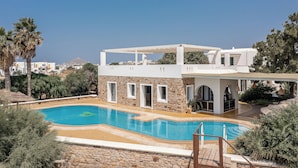 Un área de piscina moderna con un muro de piedra, una alberca y una zona de estar techada.