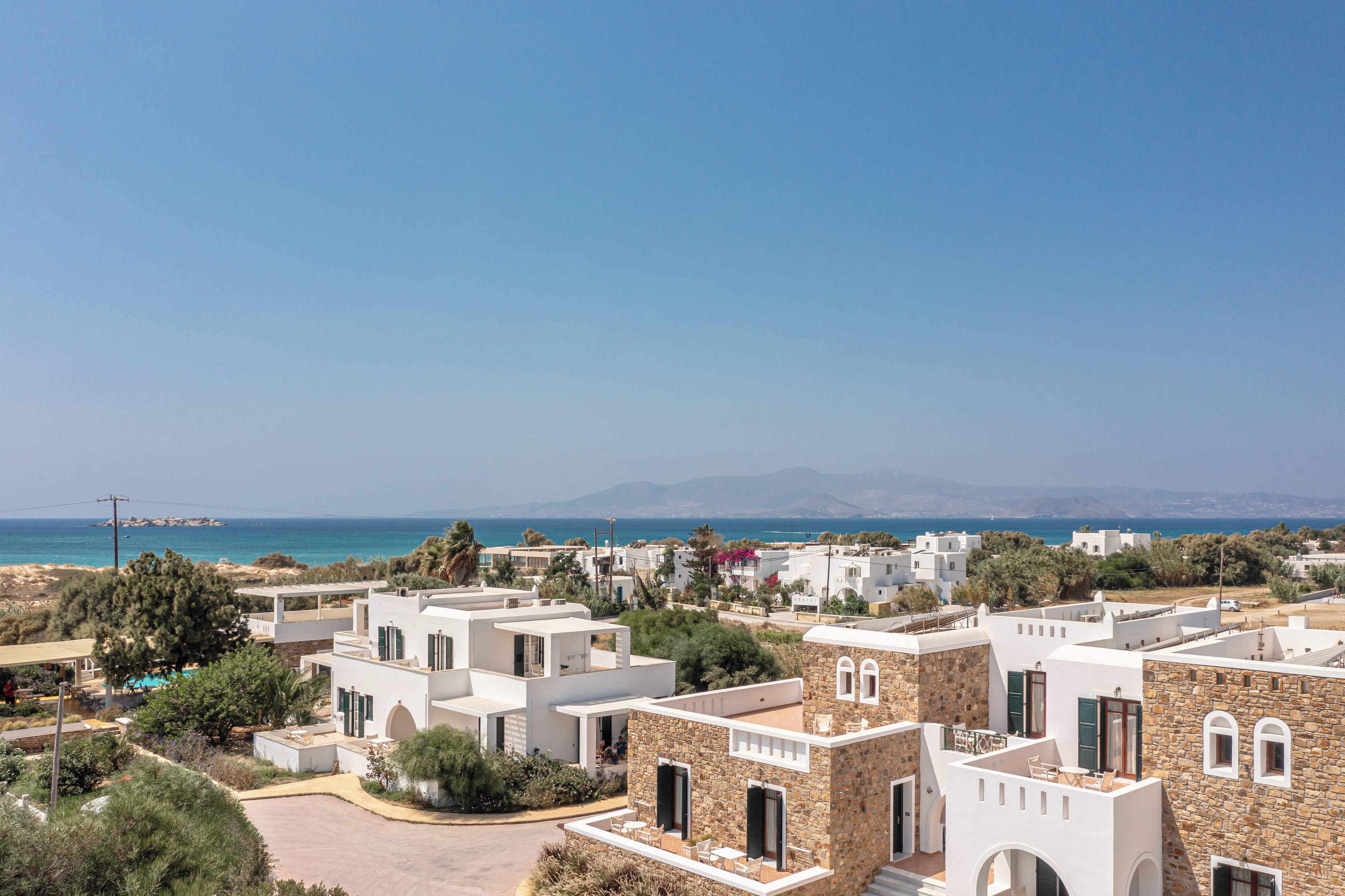 Un quartier résidentiel en bord de mer, caractérisé par des bâtiments modernes aux façades blanches, dont certaines sont en pierre, et offrant une vue dégagée sur la mer et les montagnes lointaines.