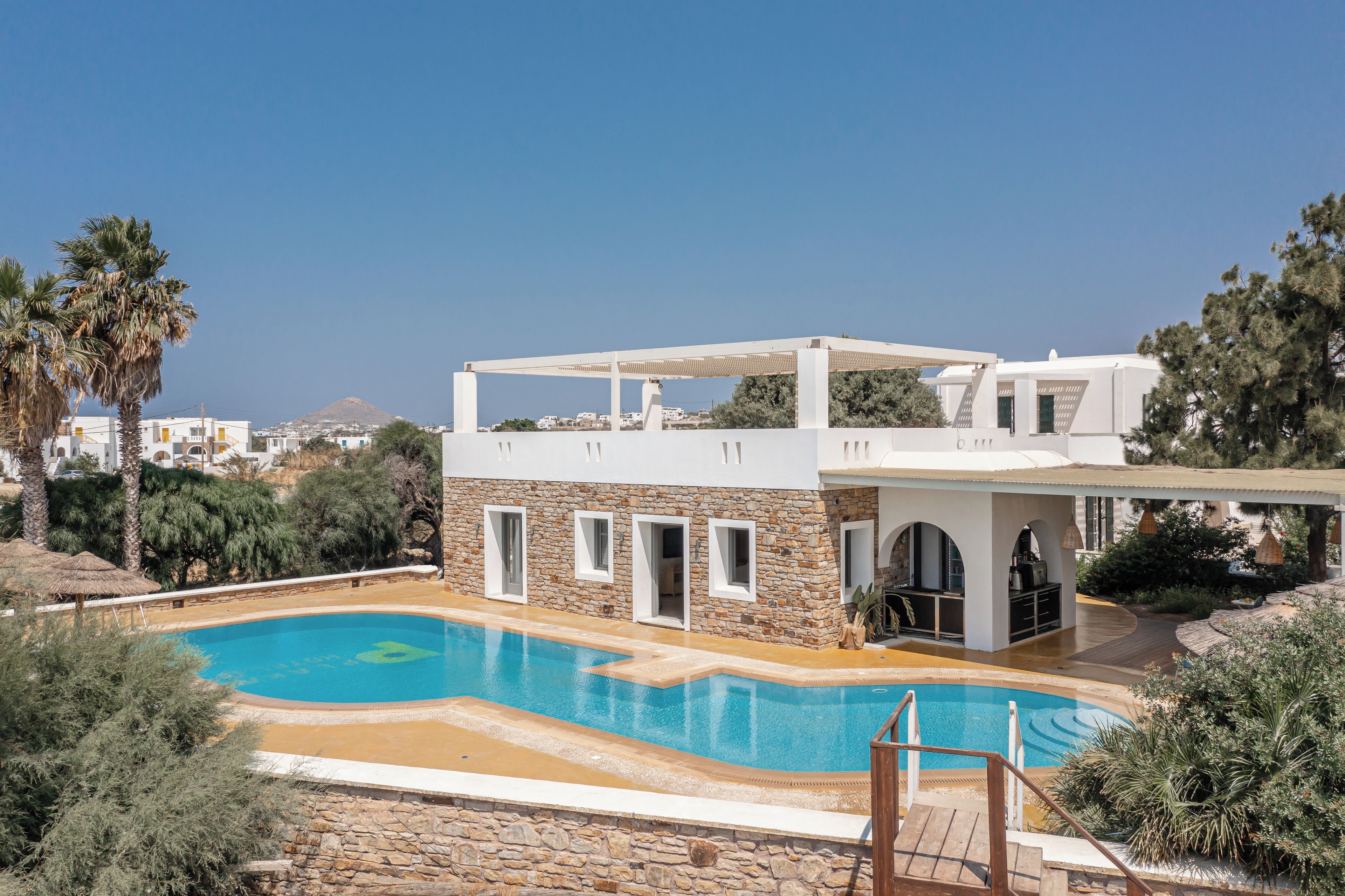 Un espace moderne aménagé au bord de la piscine, avec un mur en pierre, une piscine et un espace salon couvert.