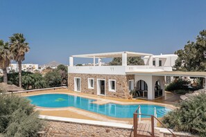 A modern poolside area with a stone wall, a pool, and a covered seating area.