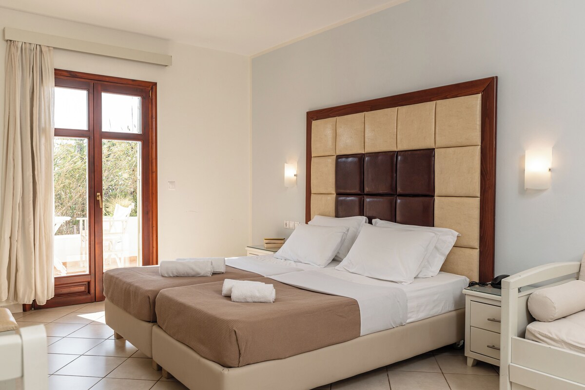 A double bed with a wooden headboard, two bedside tables, a nightstand, and a view of the outdoors through a sliding glass door.