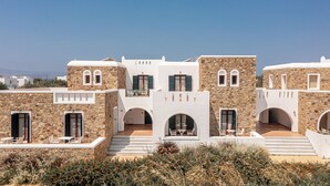 Un edificio moderno con muros de piedra y balcones blancos, que cuenta con zonas de estar al aire libre y arcos de entrada.