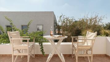 A terrace with two white chairs and a small round table, a bottle, and two wine glasses.