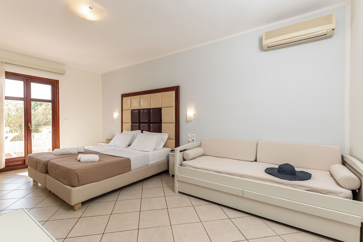 A bedroom with two beds, a sofa, an air conditioning unit, and a window with curtains.