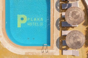 An aerial view of a swimming pool with 'PLAKA HOTEL II' written in the water, surrounded by sun loungers and umbrellas.