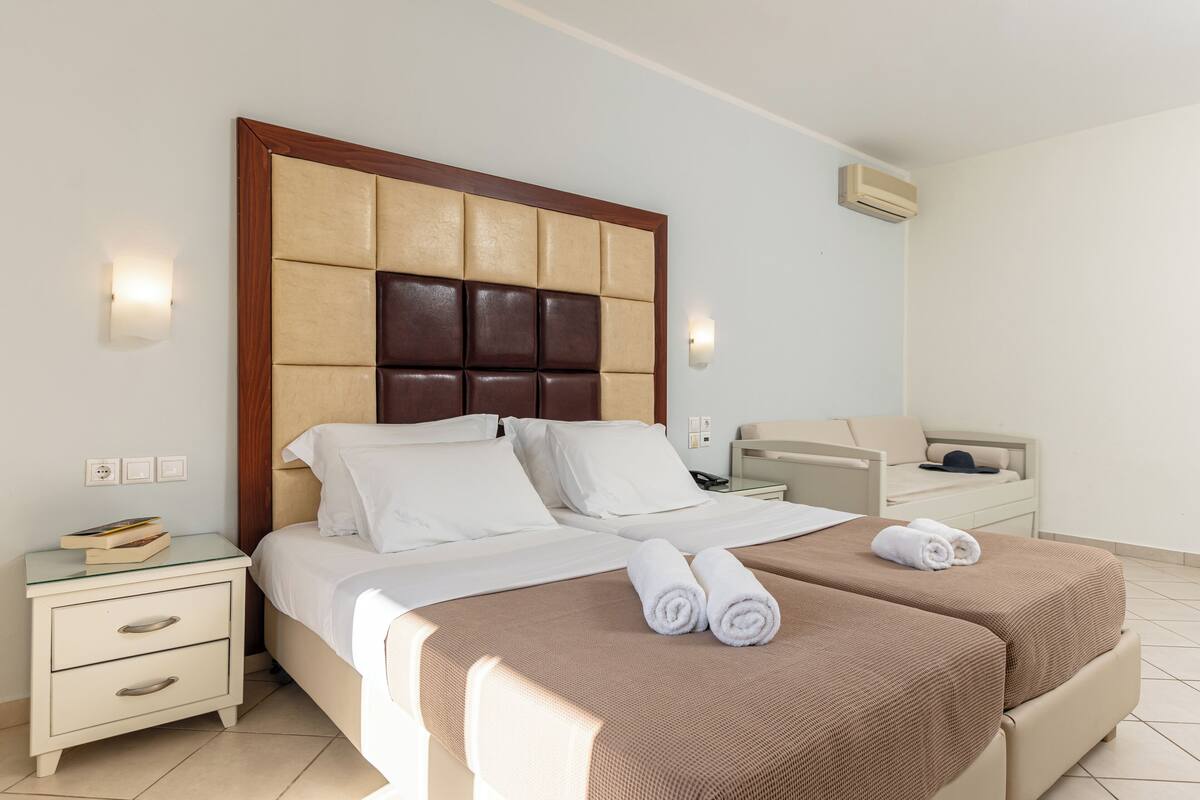 Ein Hotelzimmer mit einem großen Bett, zwei Nachttischen, einem Spiegel und einer wandmontierten Klimaanlage.