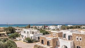 Zona residencial costera con edificios blancos modernos, algunos con fachadas de piedra, y una vista despejada del mar y montañas distantes.