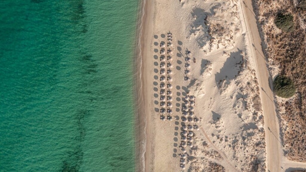 Vista aérea de una playa con hileras de sombrillas y tumbonas.