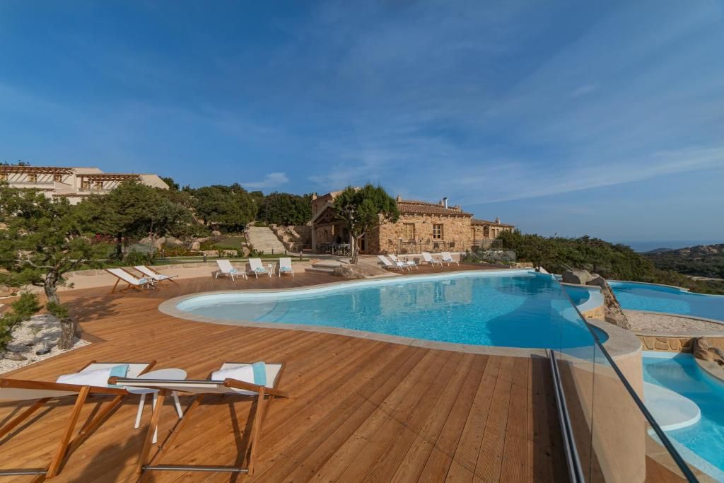 Un resort con una amplia piscina, terraza de madera y sillones de descanso.
