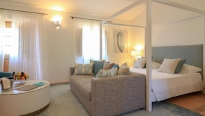 A hotel room with a bed, a sofa, a desk with a lamp, and a large window with curtains. - Hotel Borgo Smeraldo (Olbia)