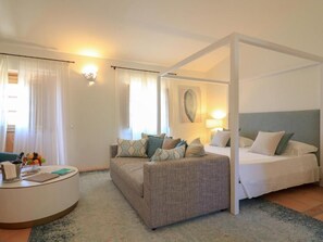 A hotel room with a bed, a sofa, a desk with a lamp, and a large window with curtains. - Hotel Borgo Smeraldo (Olbia)