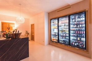 A bar area with a marble counter, two large wine refrigerators stocked with various bottles, and a hanging light fixture. - Hotel Borgo Smeraldo (Olbia)