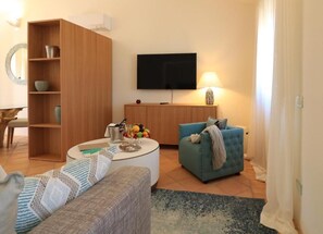 A living room with a wooden cabinet, a blue sofa, a white coffee table, and a flat-screen TV. - Hotel Borgo Smeraldo (Olbia)