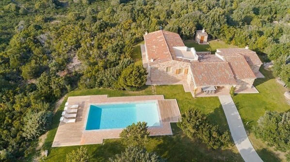 An aerial view of a property with a swimming pool, stone buildings, and a forested area. - Hotel Borgo Smeraldo (Olbia)