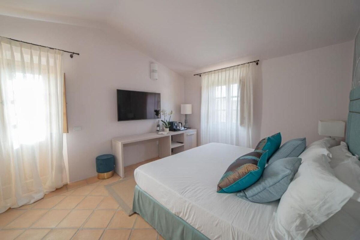 A bedroom with a bed, a desk, a TV, and curtains.