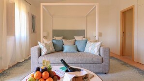 A hotel room with a grey sofa, a fruit bowl, a bottle of champagne, and a small table. - Hotel Borgo Smeraldo (Olbia)