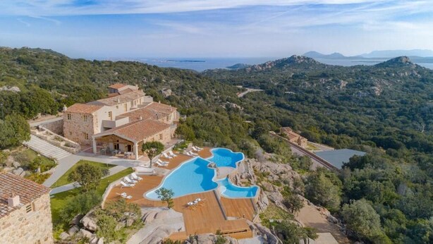 A resort with a pool, stone buildings, and a mountainous backdrop. - Hotel Borgo Smeraldo (Olbia)