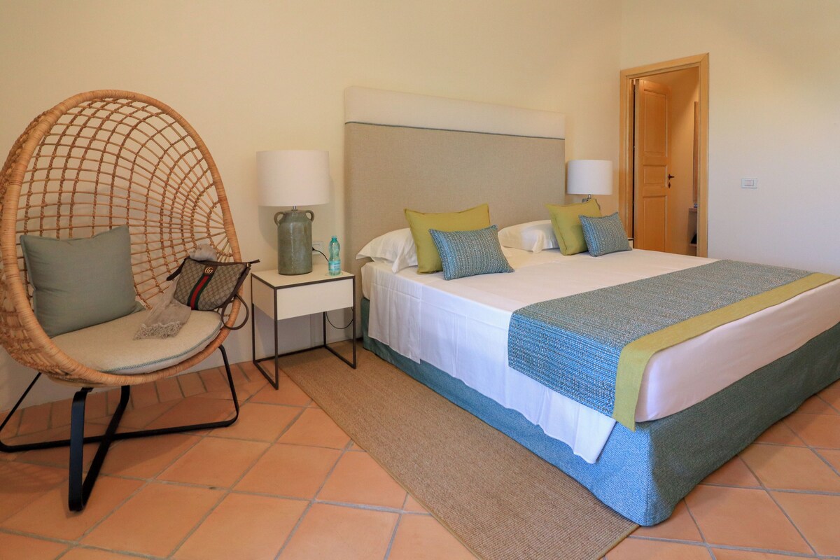 A bedroom with a bed, a chair, a nightstand, and a door.