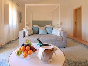 A hotel room with a grey sofa, a fruit bowl, a bottle of champagne, and a small table. - Hotel Borgo Smeraldo (Olbia)