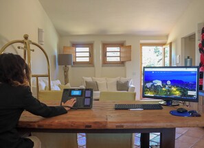 A person working at a wooden desk with a computer monitor displaying a scenic view, a lamp, and a couch in the background. - Hotel Borgo Smeraldo (Olbia)