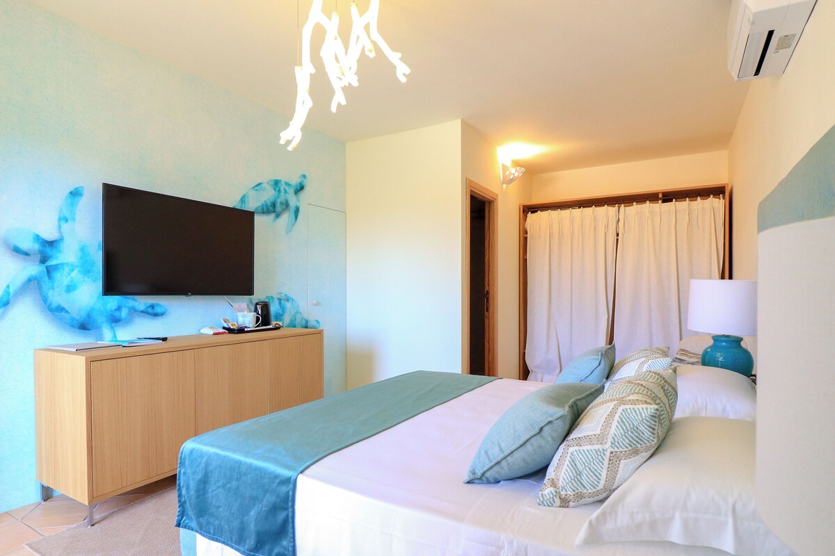 A hotel room with a bed, a TV, a wooden dresser, and a bathroom door.