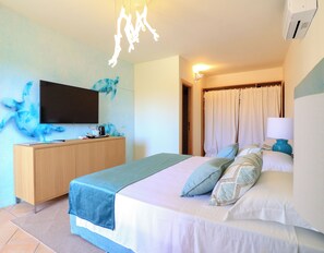 A hotel room with a bed, a TV, a wooden dresser, and a bathroom door. - Hotel Borgo Smeraldo (Olbia)