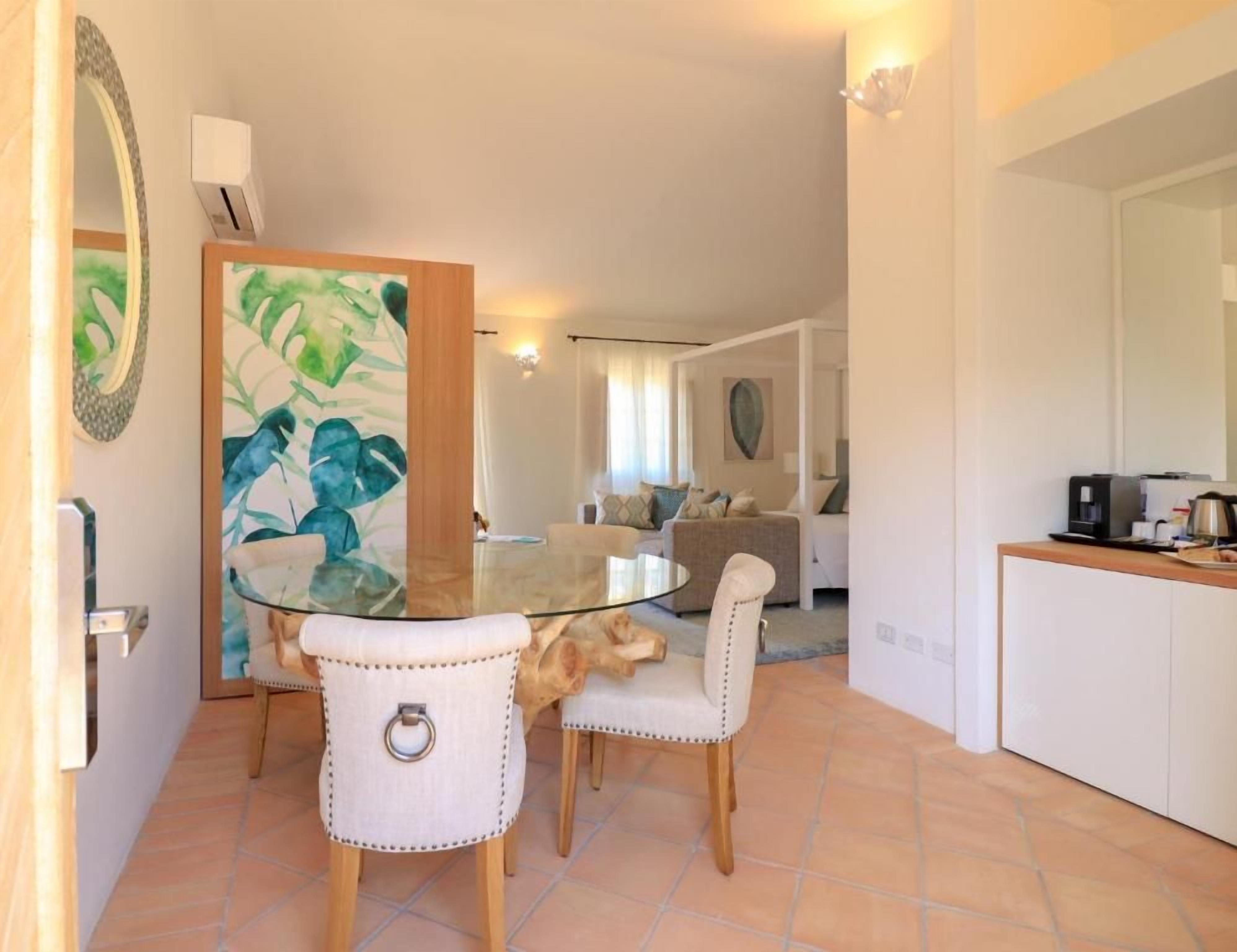 Un comedor con una mesa de vidrio y dos sillas, una zona de cocina con una cafetera y una sala de estar con un sofá y un cuadro.