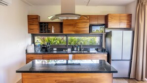 A modern kitchen with wooden cabinets, a central island, and a view of greenery outside. - Luxury Boutique Hotel Villas Jardin Caracol Tulum (Tulum)